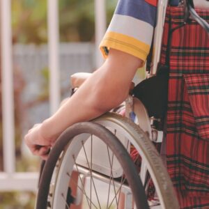 Closeup of a person in a wheelchair from the back resting their hand on the wheel of their wheelchair.