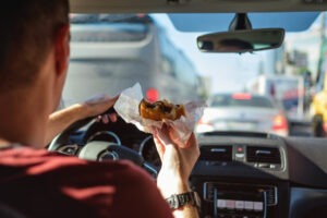 A man eating a burger with one hand driving with his other hand on the steering wheel.