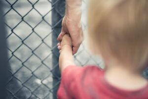A man holding the hand of his child next to a fence.