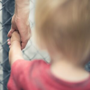 A man holding the hand of his child next to a fence.