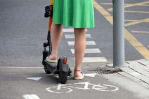 A woman riding on a lime scooter crossing the street.