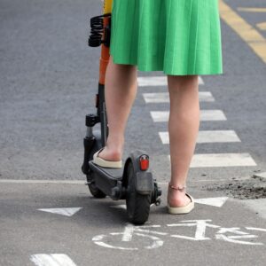 A woman riding on a lime scooter crossing the street.