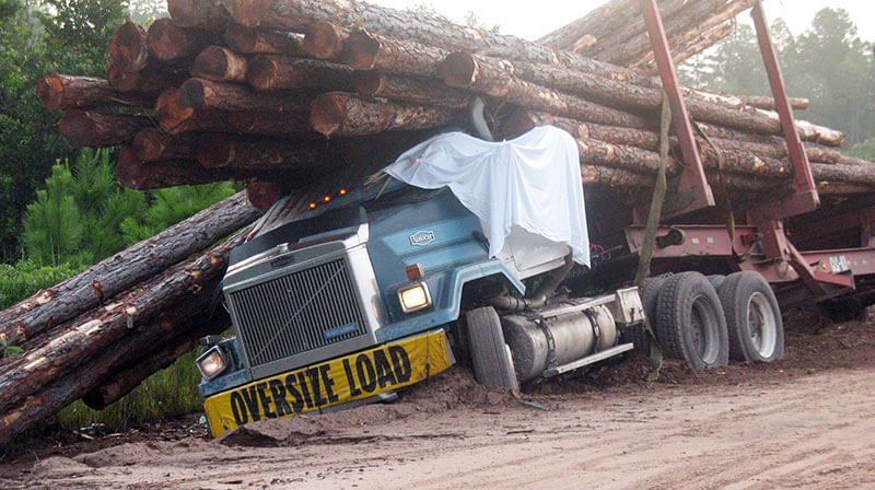 Logging truck with sign that says 'oversize load' that has toppled over