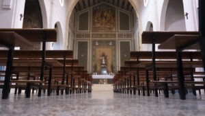 The interior of a catholic church with numerous rows of empty benches.