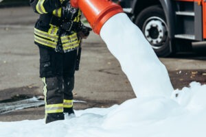 Close up of a hose spilling out firefighting foam, held by a firefighter.