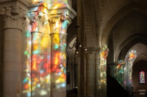 Pillars of a catholic church with colorful reflections from stained glass.