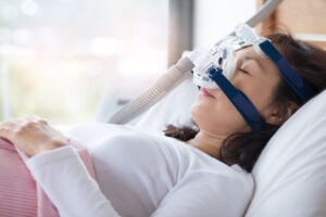 A woman laying down in a hospital bed with a CPAP machine affixed over her nose.