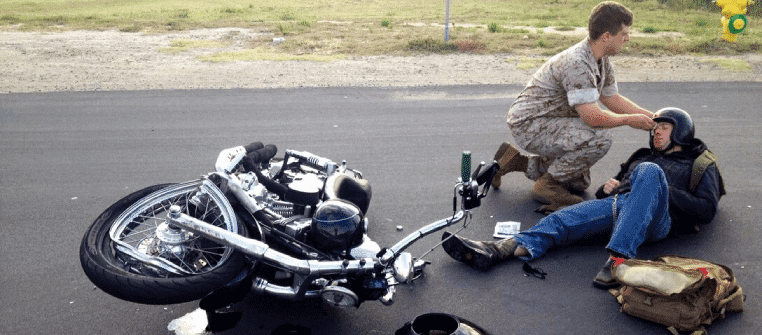 Motorcycle with injured rider on the side of the road with army man helping him out
