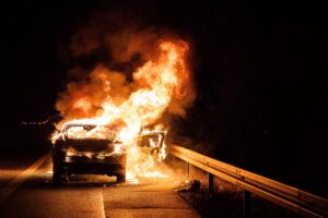 Car blazintg on fire on the side of the road at night.