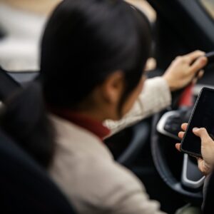 Woman driving a car while texting on her phone simultaneously.