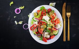 A greek salad with colorful vegetables in a white bowl.