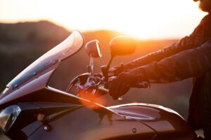 A closeup of a motorcyclist grasping his handlebars with a sunset behind.