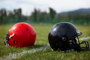 Two football helmets, one red and one black, sitting on the grass in a field.