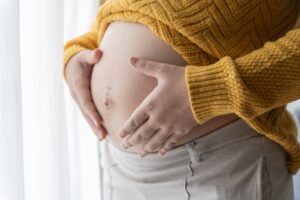 A closeup of a pregnant woman's belly being held tenderly with both hands.
