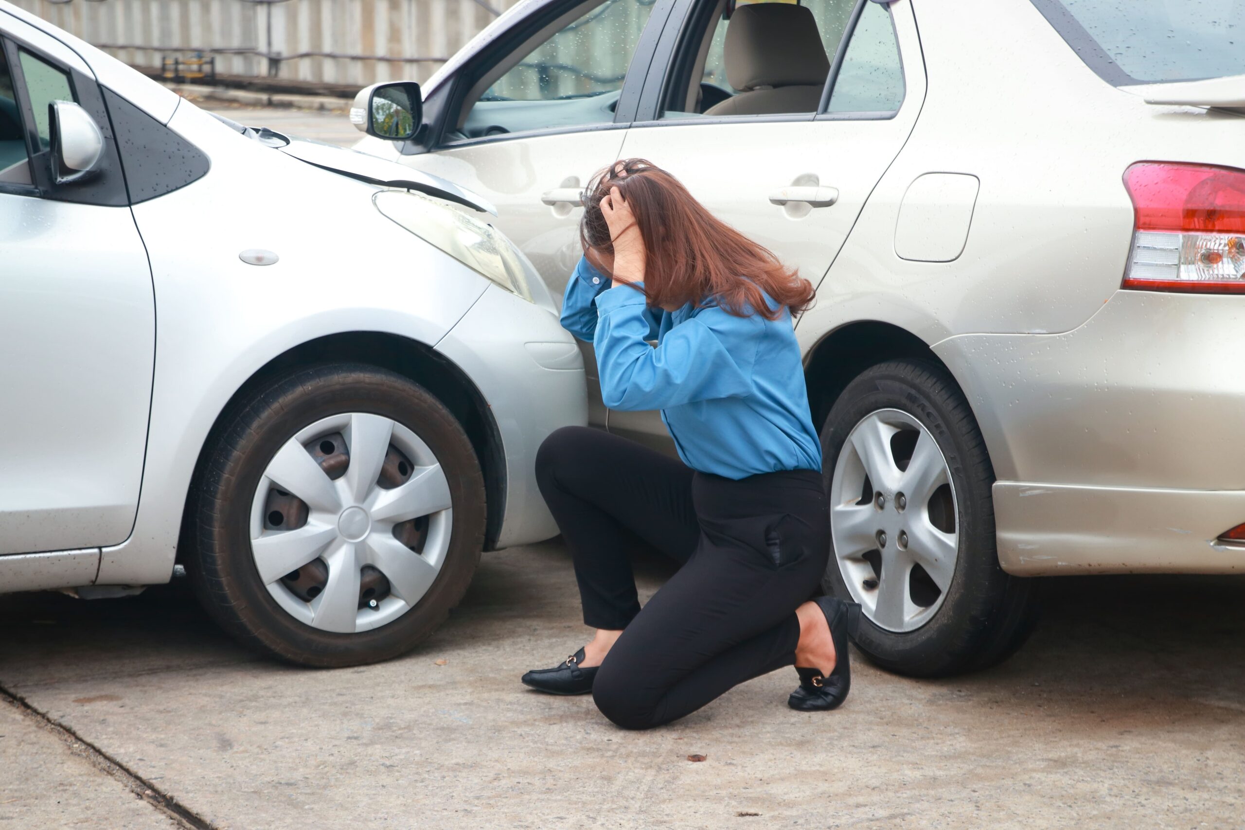 Woman grasping her head in pain next to a car accident.