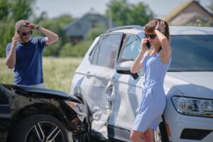 A stressed man and woman each on their phones standing next to a car accident.