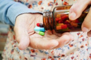 A closeup of an old woman pouring multi-colored pills into her hand.