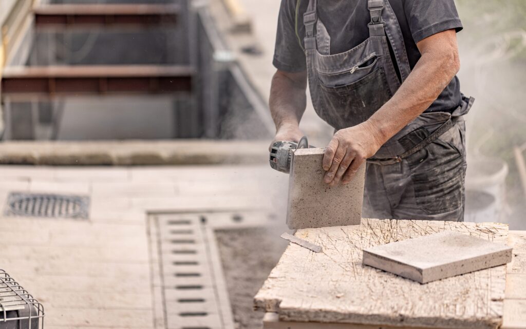 A worker cutting concrete, causing hazardous silica dust to rise.