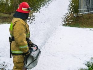 A firefighter using firefighting foam to douse a fire.