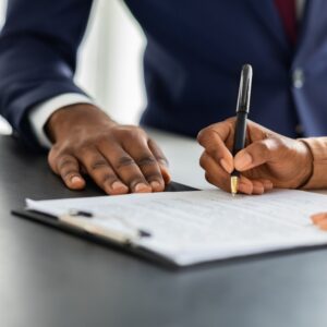 A woman signing a piece of paperwork next to her lawyer.