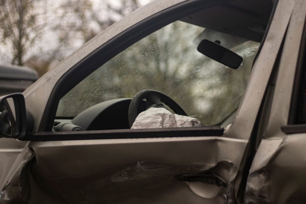 A grey car with dents and an open air bag follwing a car accident.