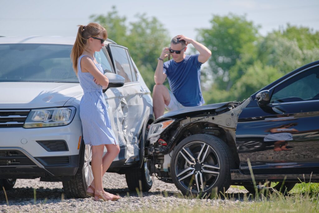 A woman and man standing next to their respective cars that were just in a t-bone accident.