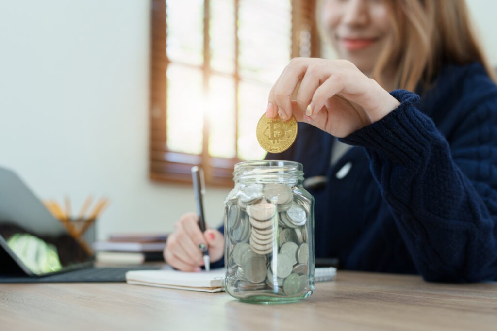 A woman dropping a crypto coin into a savings jar.