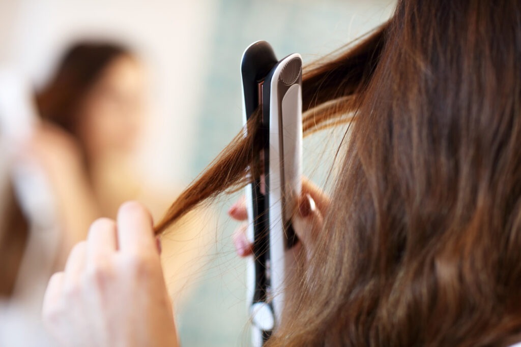 A closeup of a woman standing straightening her hair.