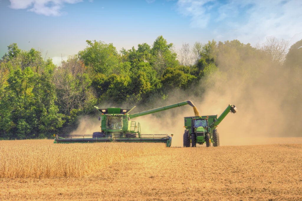 A tractor driving across a farm causing dust to rise into the air.