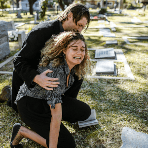 A man comforting a crying woman in a graveyard.