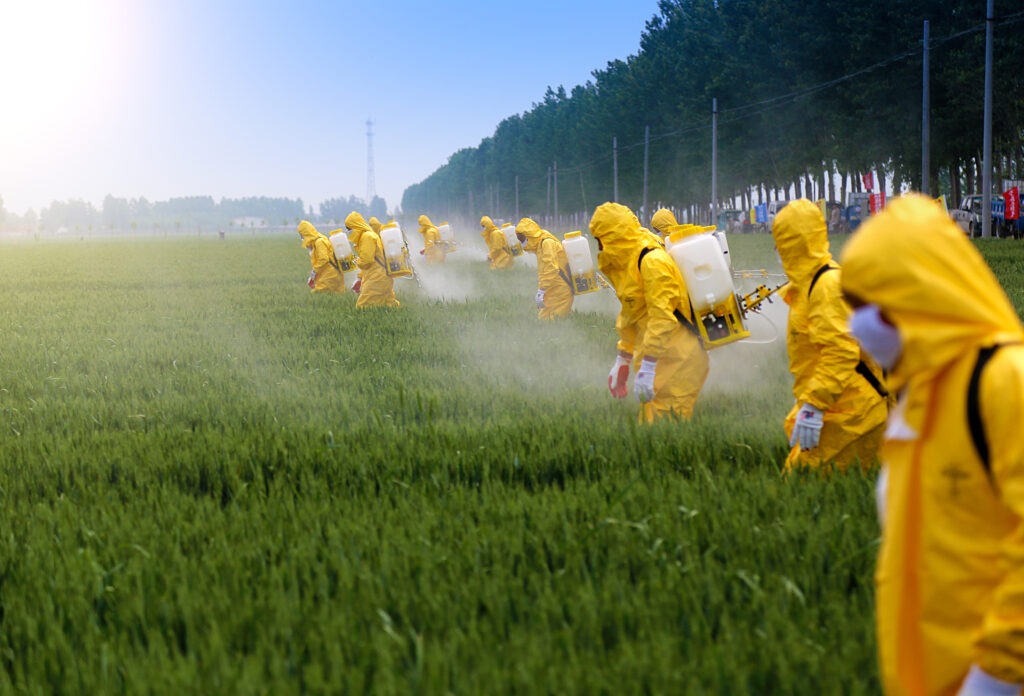People spraying crops with pesticides in full body suits.