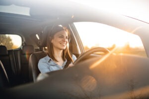 Young woman driving a car with rays of sunshine glaring through her windshield.