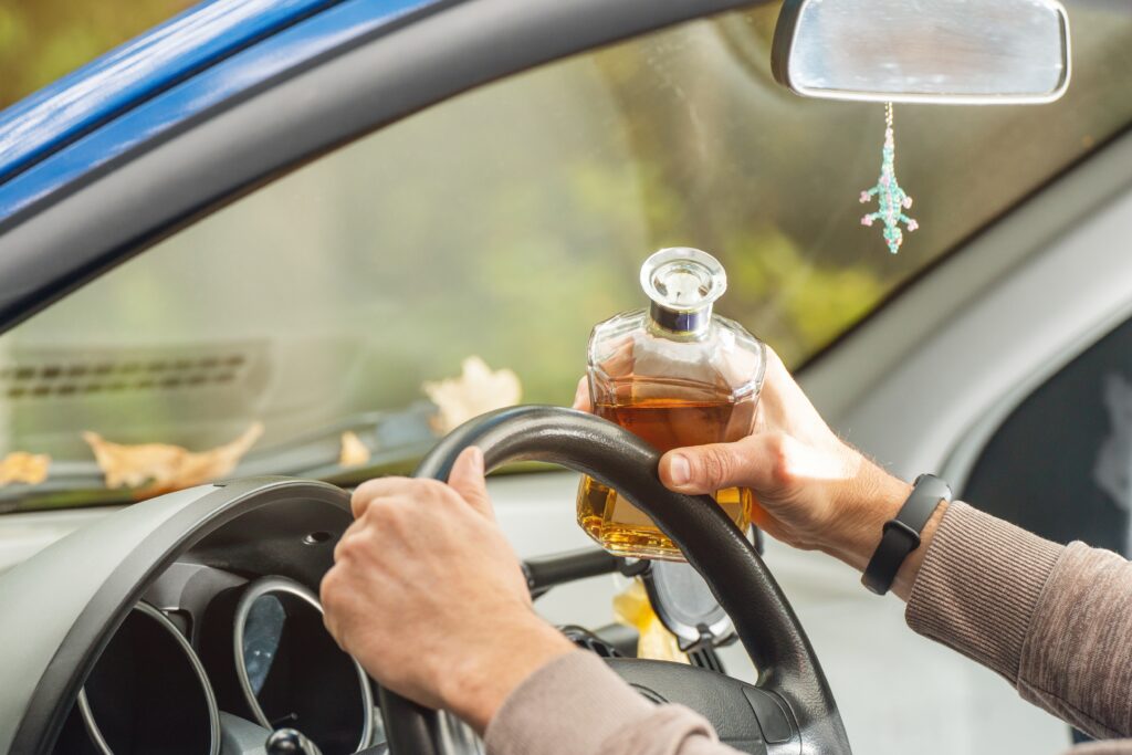 Person driving with glass of alcohol in hand.