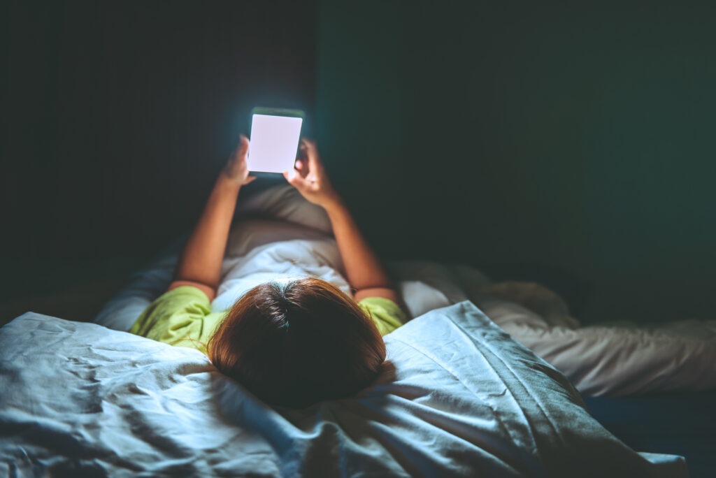 A woman looking at her glowing cell phone in bed.
