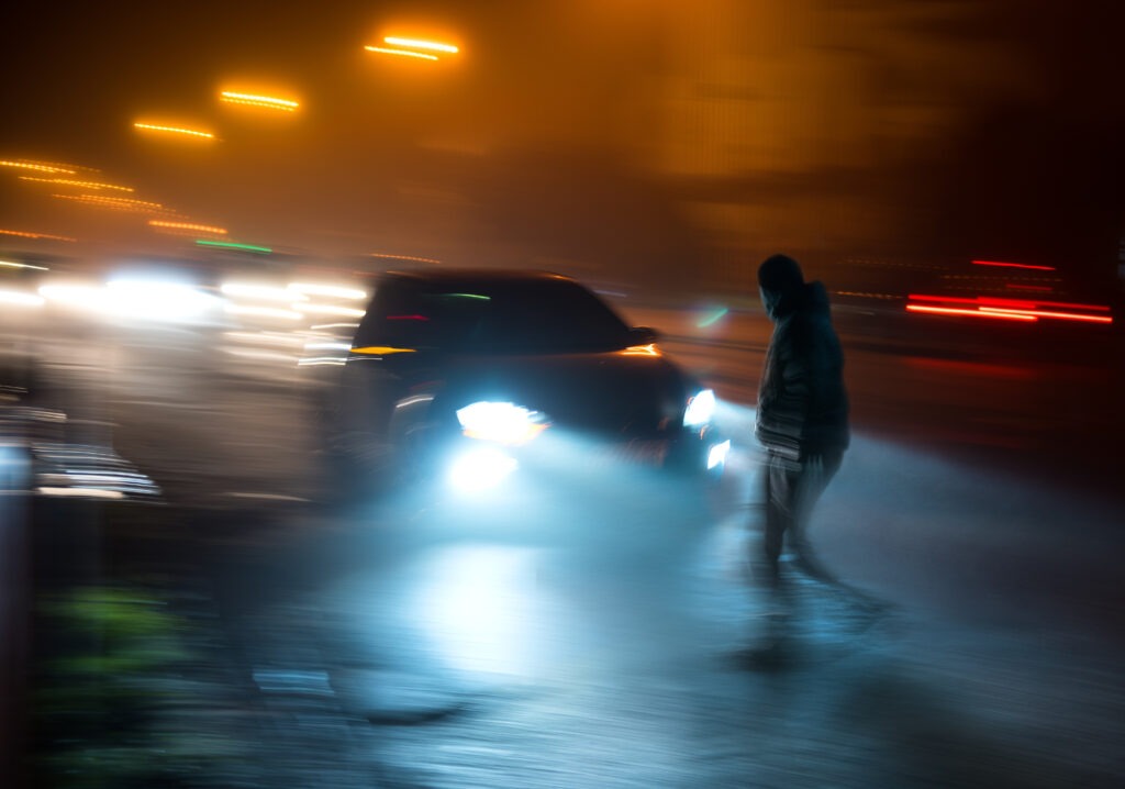 A car swerving into a pedestrian crossing the street at night.
