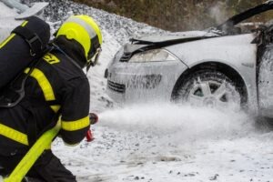 A firefighter extinguishing a car fire with foam.