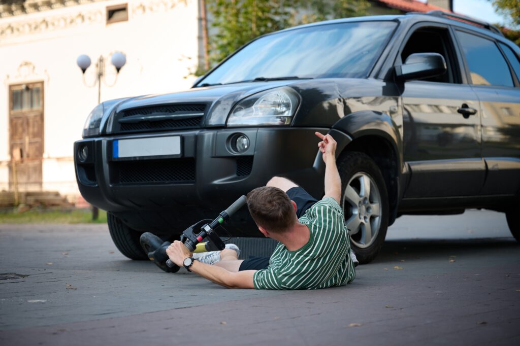 A man fallen on the concrete after being struck by a car while on his scooter.