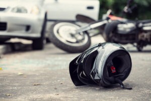 A motorcycle helmet lying on the side of the road with a blurred car and motorcycle in the background.
