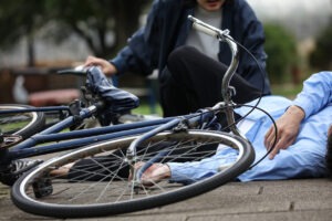 A fallen bicycle rider on the pavement following a bicycle accident.