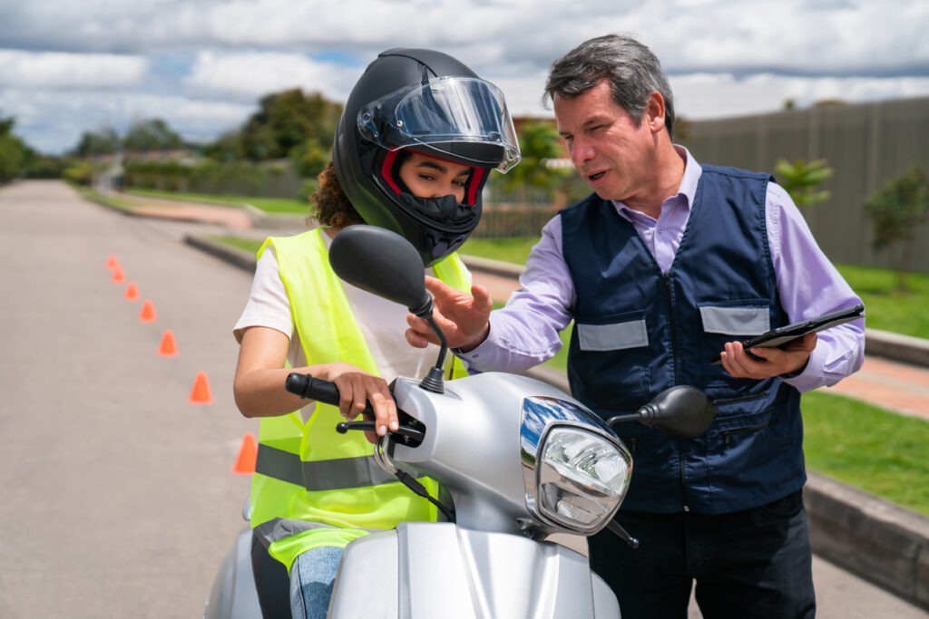 A woman learning to drive a motorcycle from an instructor.