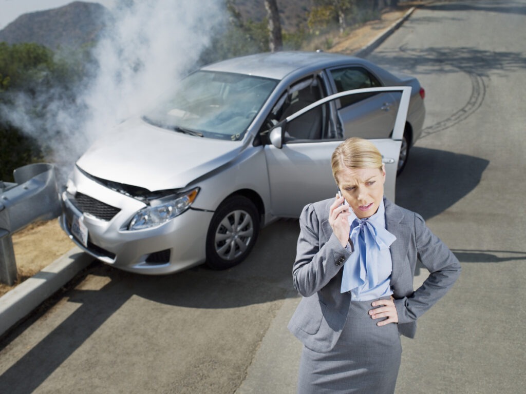 A business woman standing next to her totaled car after an accident.