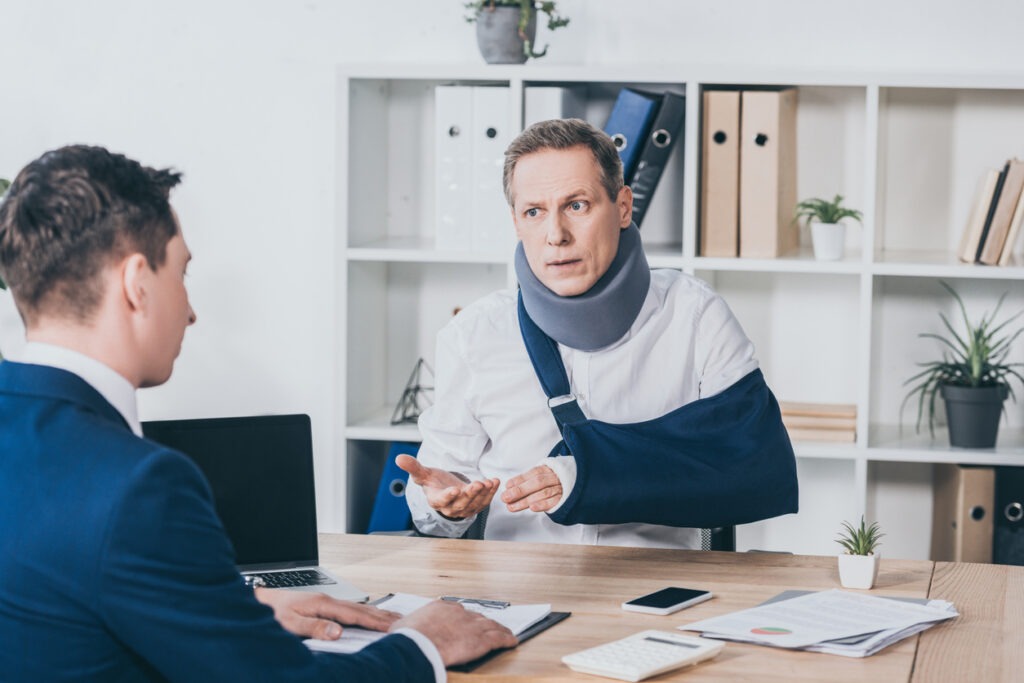 Injured man in neck brace with arm in sling discussing his lawsuit with a lawyer.