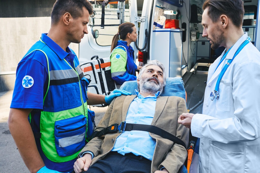 A man sat in a stretcher outside of an ambulance with a doctor to his left and a paramedic to his right.