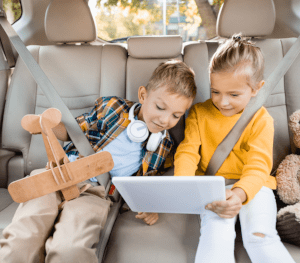 Two kids smiling at a tablet in their car.