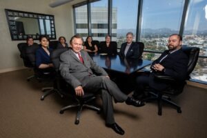 A group of smiling lawyers sat around a table in black chairs looking toward the camera.