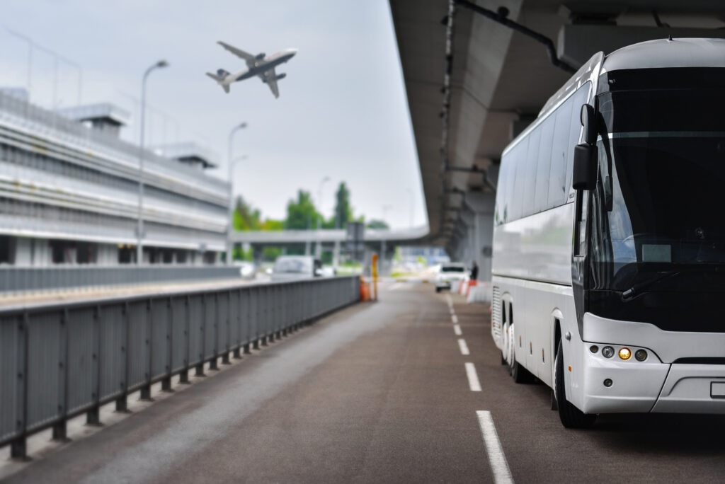 An LAX shuttle bus driving on the road with a blue sky and plane flying overhead in the background.