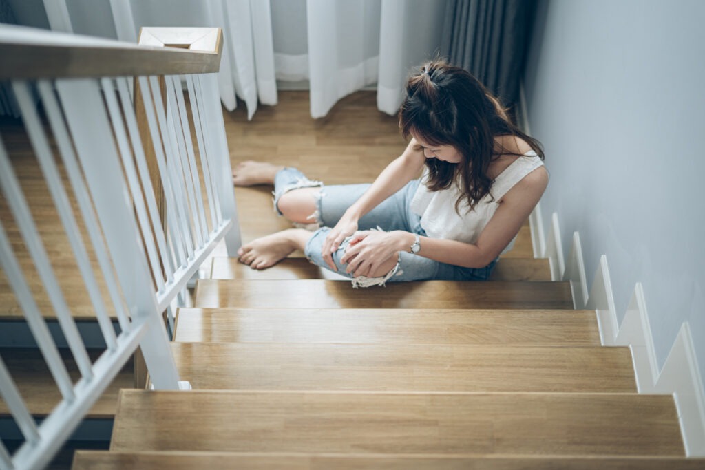 A woman clutching her injured knee at the bottom of a flight of stairs in a rental home.