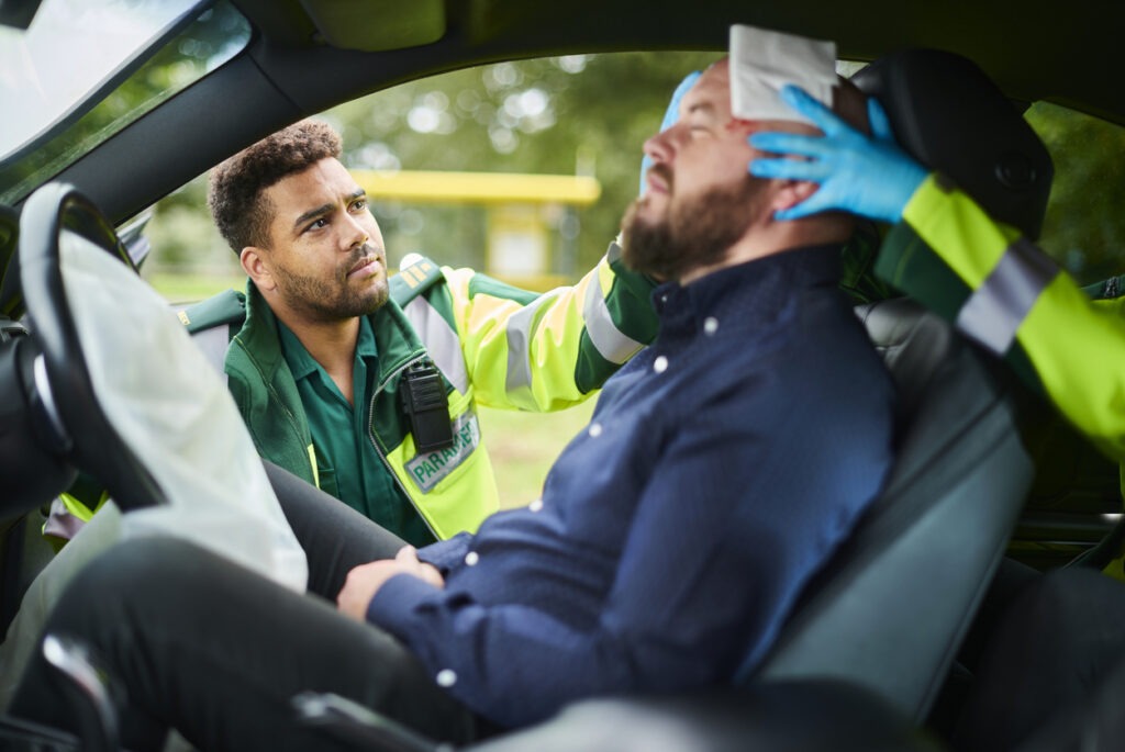 Paramedics icing the head of a man in the drivers seat of a car crash.