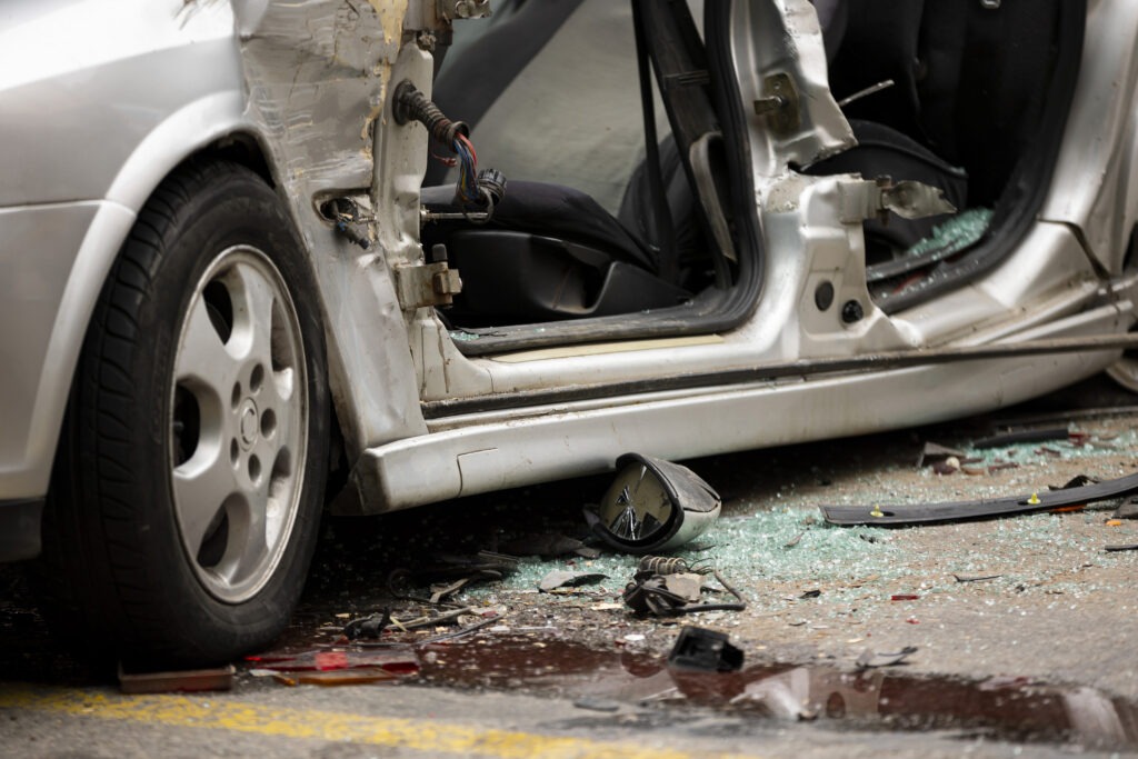 A silver totaled car with a missing  door following a disastrous car accident.