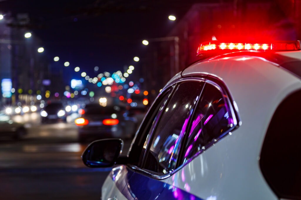 A police car with its lights on preparing to pursue a car that perpetrated a hit-and-run.